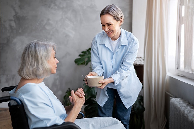 NYHC's CDPAP for Consumers - The CDPAP caregiver is helping an older patient have her meal, showing NYHC's commitment to quality care.