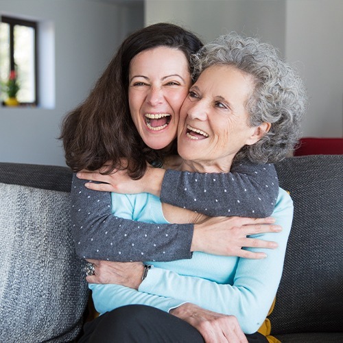 NYHC's Companion Care service for seniors: Our caregiver warmly embracing an elderly woman, both sharing smiles and enjoying quality time together, showing compassionate and joyful companionship in senior care.