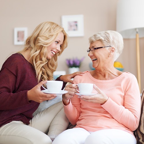 NYHC's Personal Care service for seniors: An elderly woman enjoying quality time with our caregiver, sharing tea in a comfortable environment.