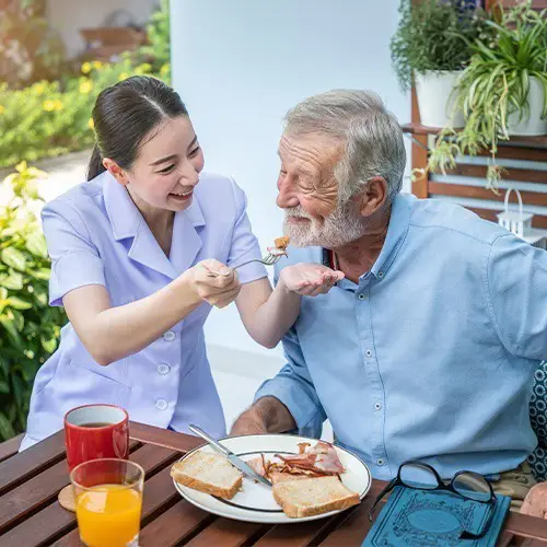 NYHC's Private Duty Nurse assisting an elderly individual with their meal, both sharing smiles in a supportive environment