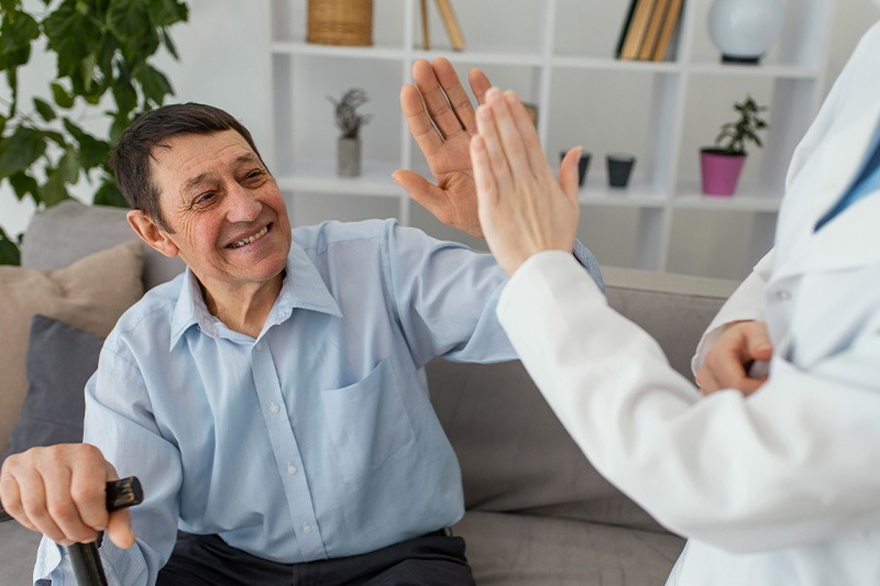 NYHC's CDPAP caregiver is sharing joy with an elderly person. They both give a high-five to each other, reflecting NYHC's commitment to compassionate care