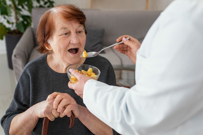 NYHC's CDPAP caregiver is helping an older patient with eating a meal. It shows how the NYHC team ensures care for consumers while helping them in their daily activities